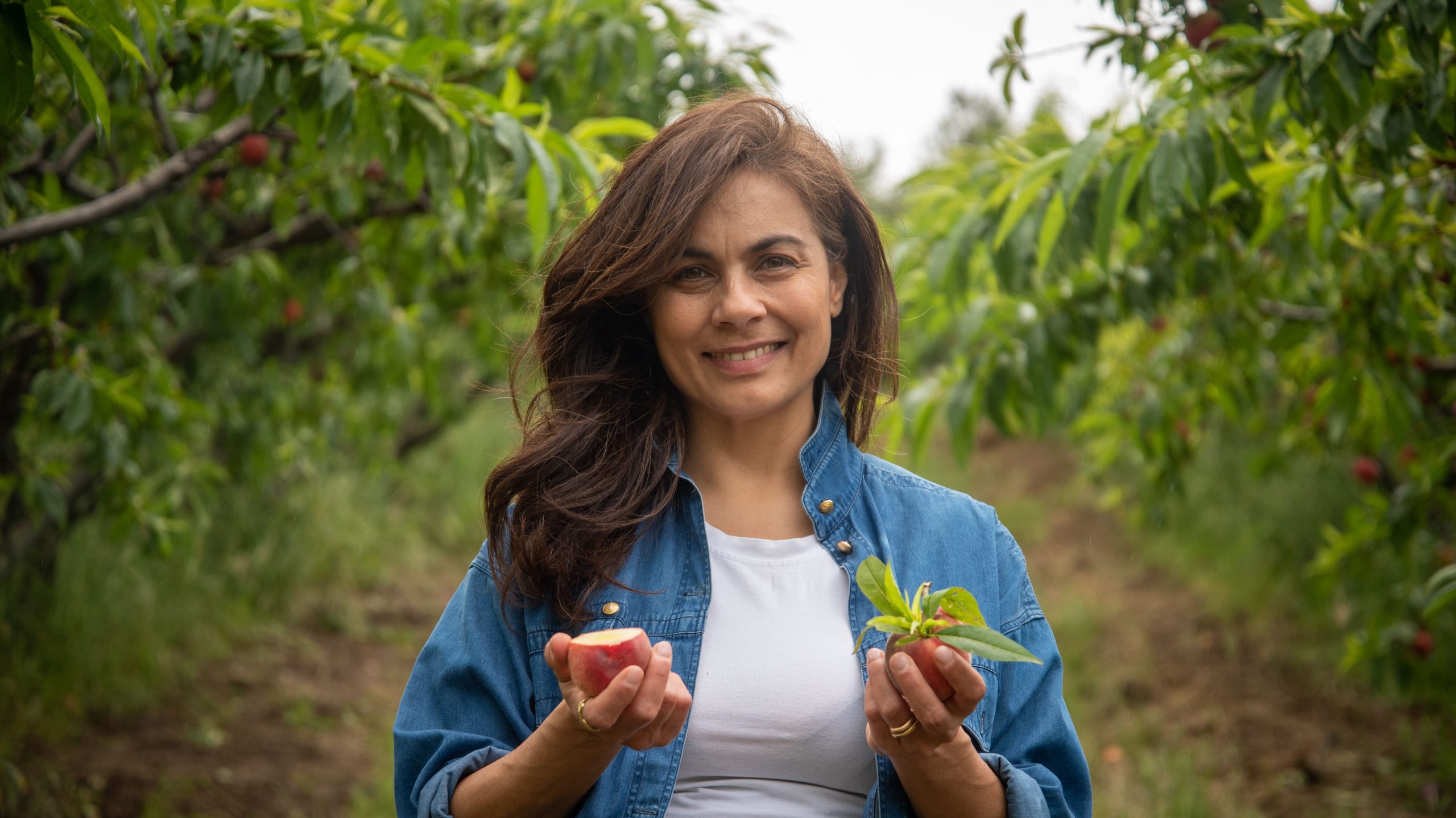 Woman farmer holding summer fruit with trees behind